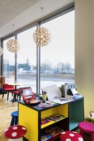 A modern children's play area with colorful furniture, a desk with educational materials, and large windows offering a view of the outside.