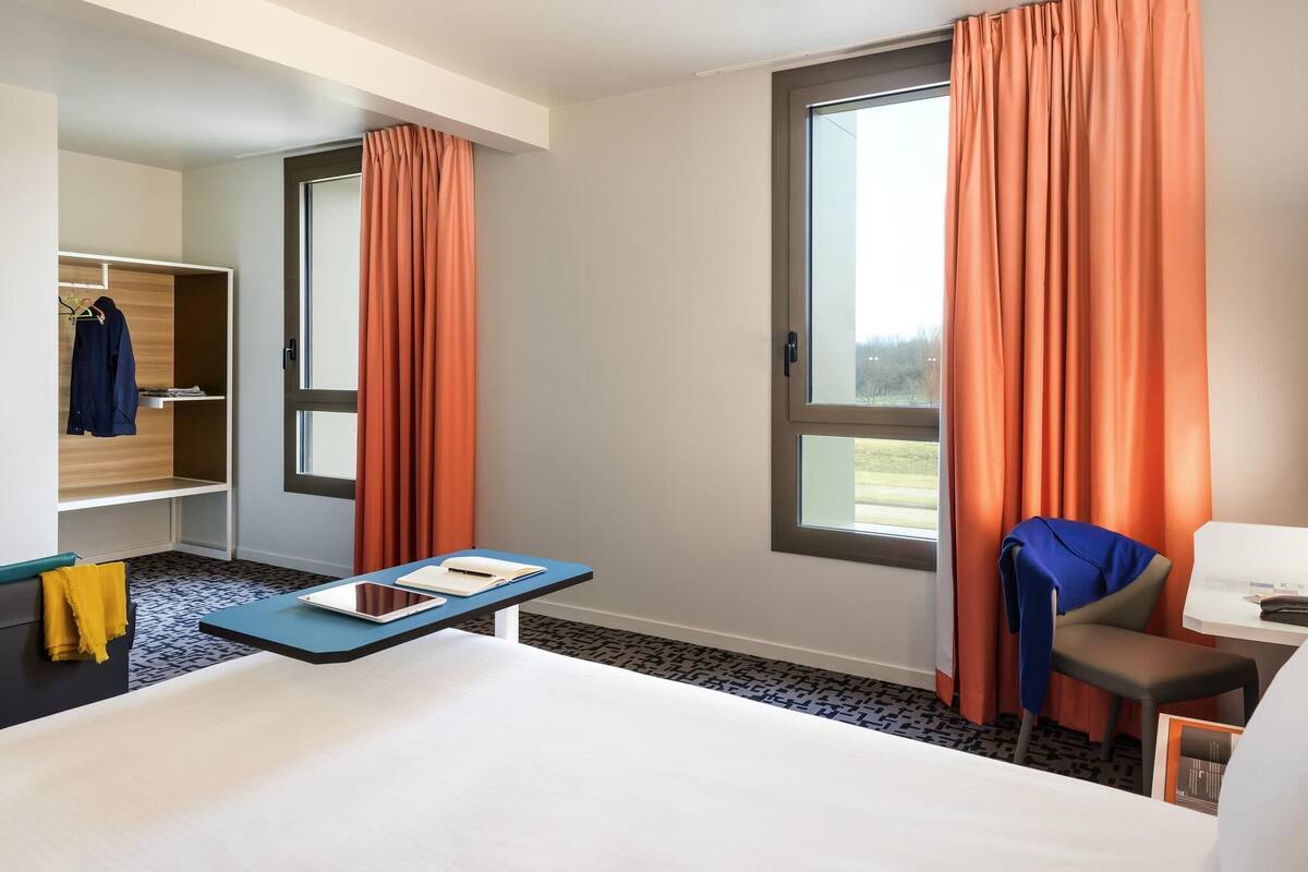 Hotelkamer met een bed, een bureau met stoel, een kledingkast en een raam met gordijnen.