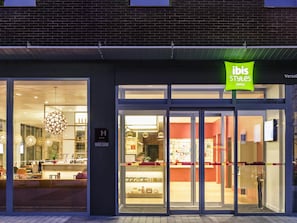 A hotel entrance with glass doors, a reception desk, and a sign for 'ibis Styles Hotels'.