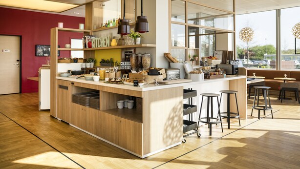 Un café moderne avec un comptoir en bois, des tabourets de bar et une variété de produits alimentaires exposés sur des étagères.