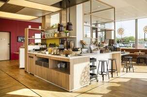 A modern cafe with a wooden counter, bar stools, and a variety of food items displayed on shelves.