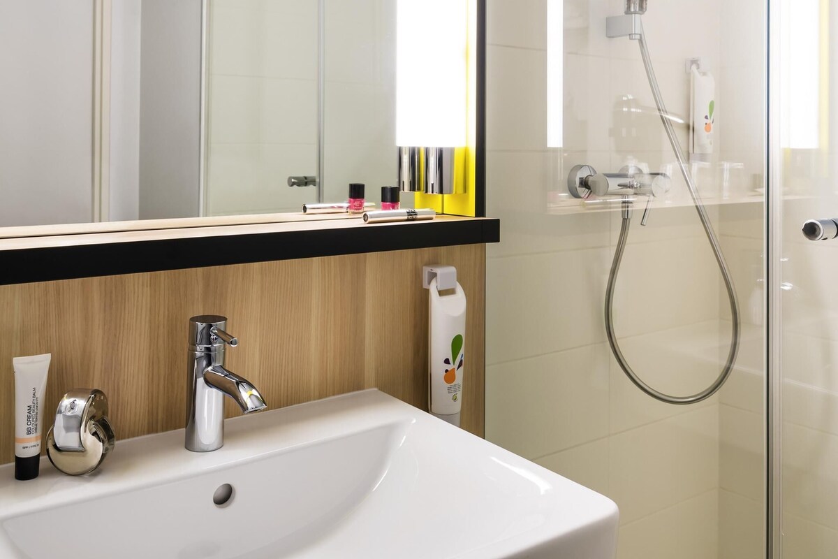 Ein Badezimmer mit weißem Waschbecken, Chromarmatur und einer Duschkabine aus Glas.