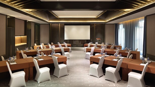 A conference room with a large screen, multiple tables, and chairs arranged for meetings.