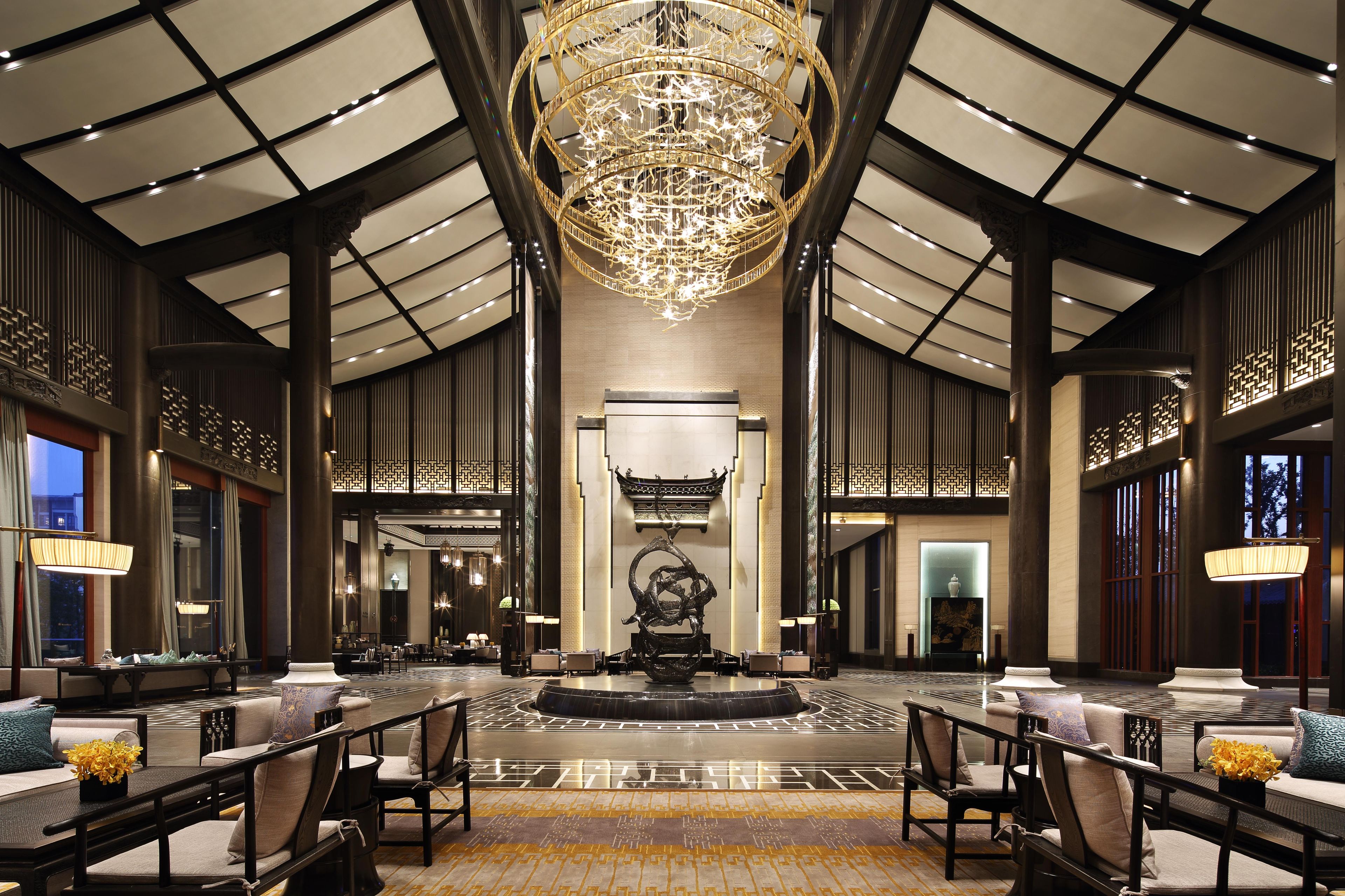 Un hall d’entrée spacieux, agrémenté d’un grand lustre, de coins salon et d’une pièce décorative centrale.