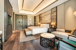 A modern hotel room with a large bed, a sofa, a round coffee table, and a desk.
