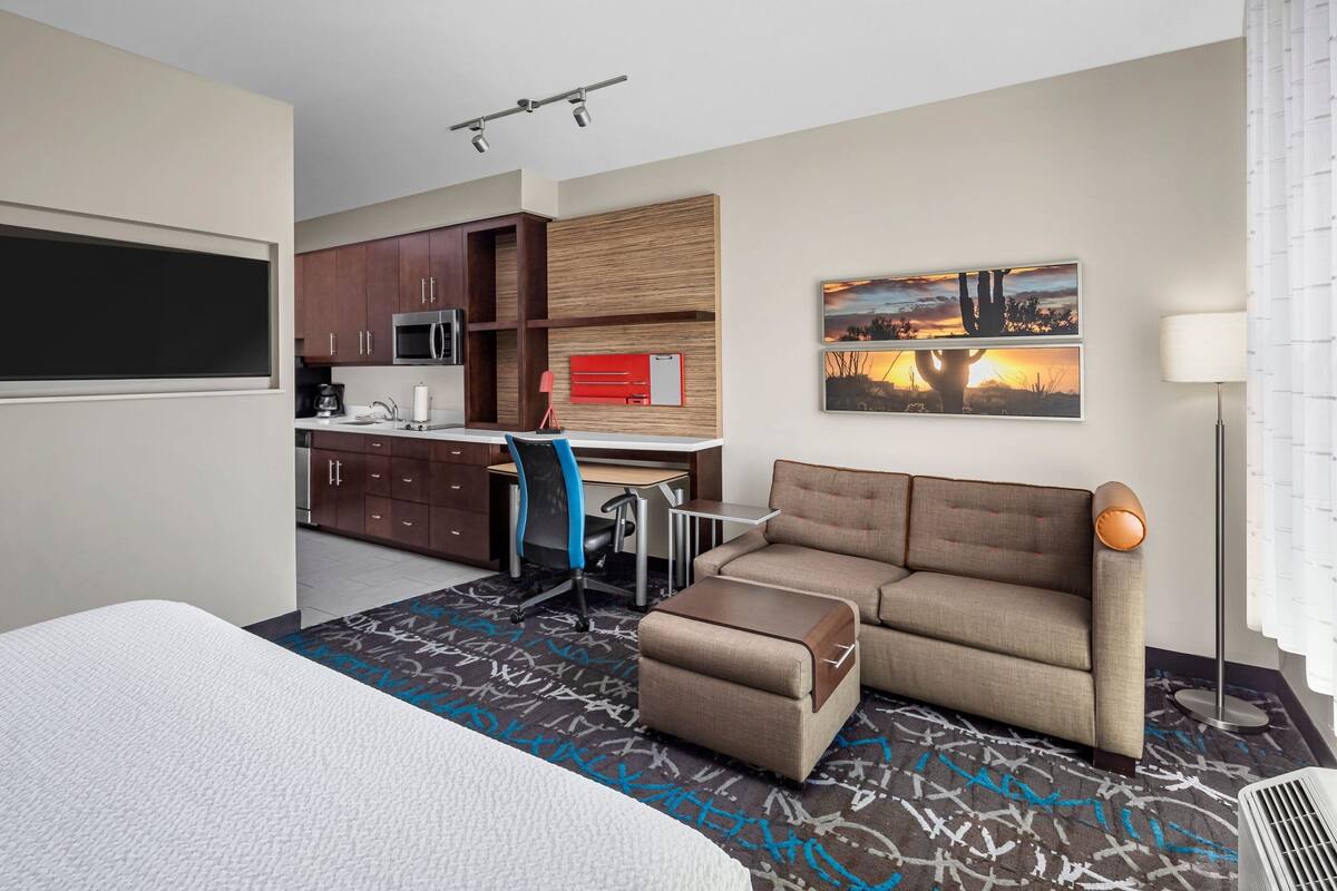 Una habitación de hotel moderna con cama, sofá, escritorio con silla, microondas y un armario rojo.