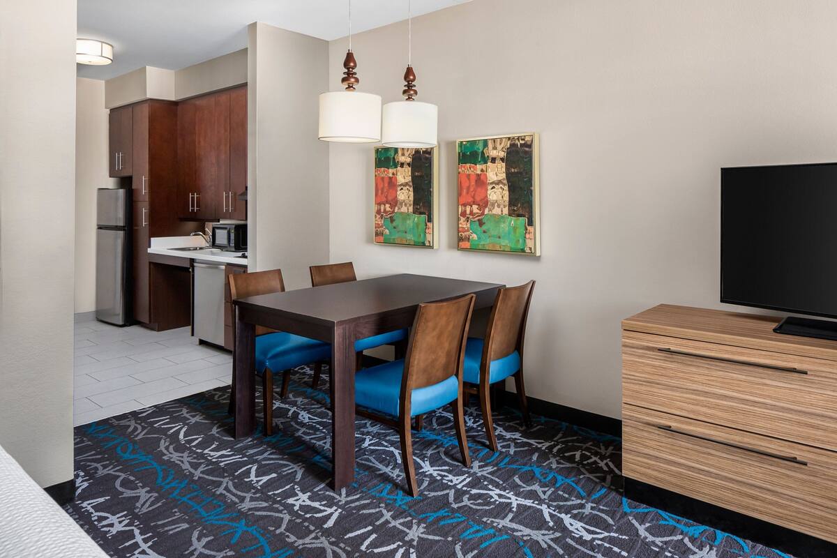 Una habitación de hotel con una mesa de comedor, sillas, televisor, microondas y armarios.