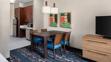 Una habitación de hotel con una mesa de comedor, sillas, televisor, microondas y armarios.