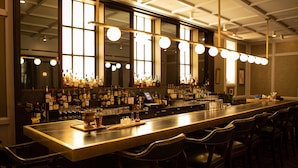 A bar with a long counter, multiple bottles, glasses, and a few chairs. - The LINE Hotel DC (Washington)