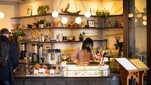 A bakery counter with pastries and coffee equipment, shelves with plants, and a person preparing food. - The LINE Hotel DC (Washington)