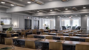 A spacious conference room with multiple tables and chairs, equipped with glassware and notebooks, and featuring a fireplace and large windows. - The LINE Hotel DC (Washington)