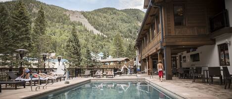 A pool area with lounge chairs, a wooden building with balconies, and a mountainous backdrop.