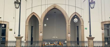 A building with three arched doorways, a balcony with a metal railing, and hanging light fixtures.
