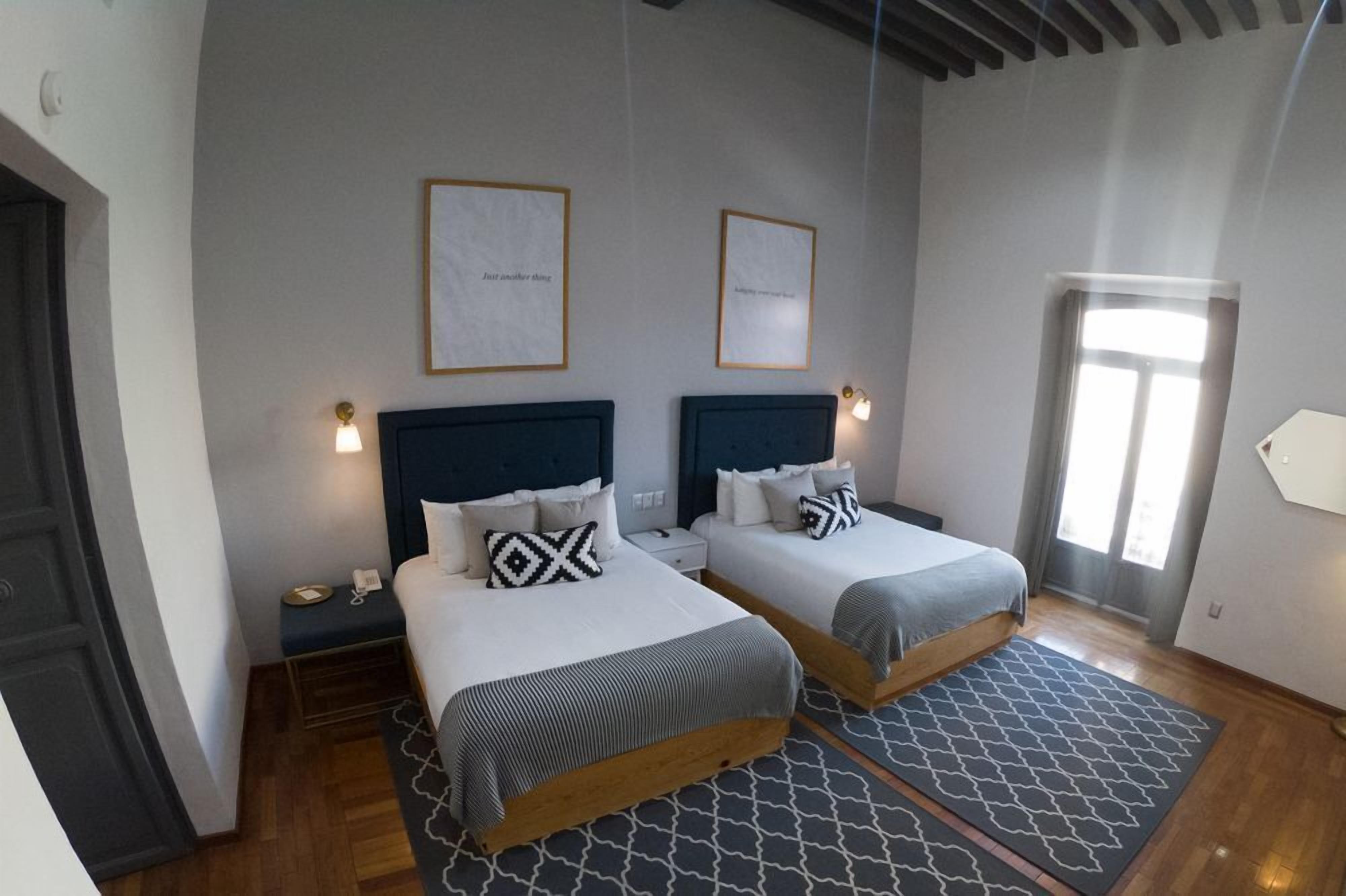 Habitación de hotel con dos camas, una mesita de noche con lámpara, una puerta y una ventana.