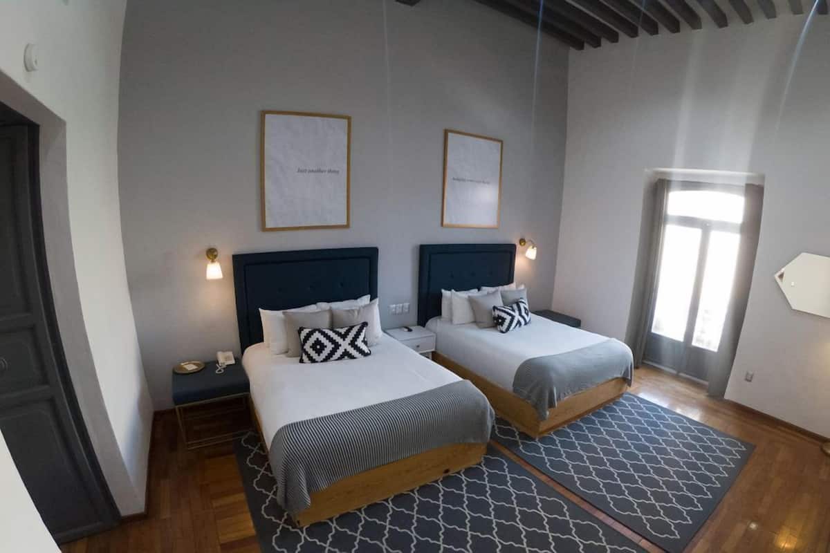 Une chambre d’hôtel avec deux lits, une petite table de chevet avec une lampe, une porte et une fenêtre.