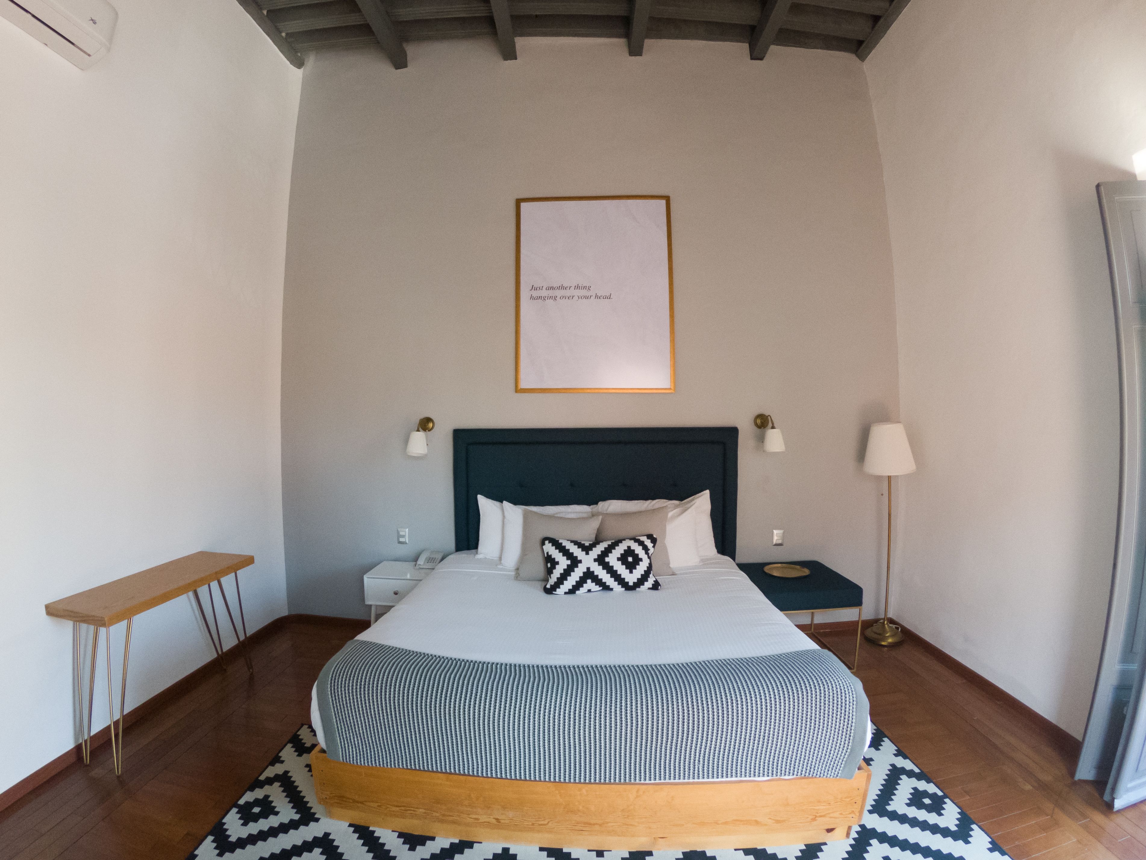 A neatly arranged bedroom with a bed, bedside tables, a bedside lamp, a framed quote on the wall, and a patterned rug.