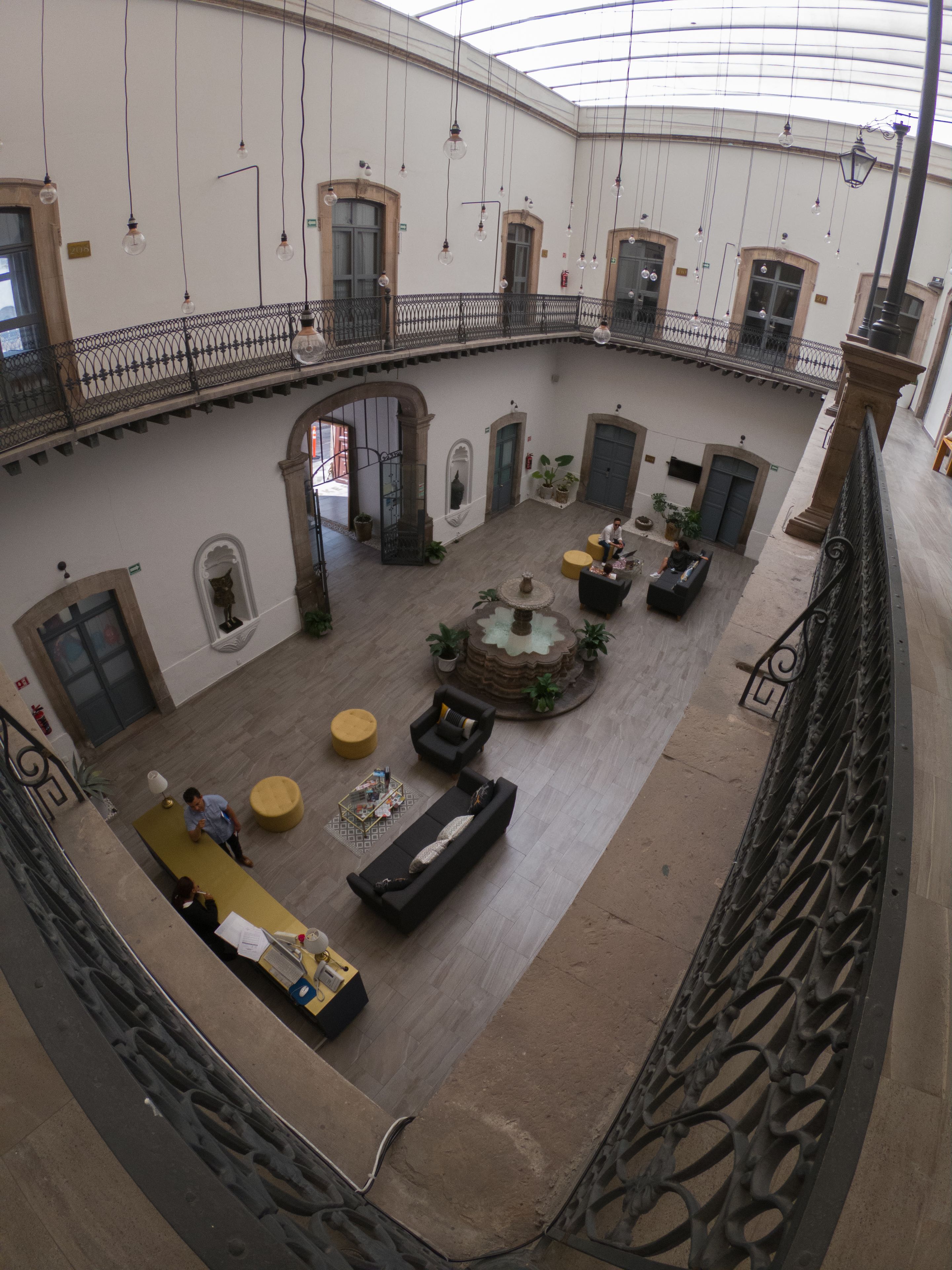 A spacious atrium with a central fountain, seating areas, and a balcony with a wrought iron railing.