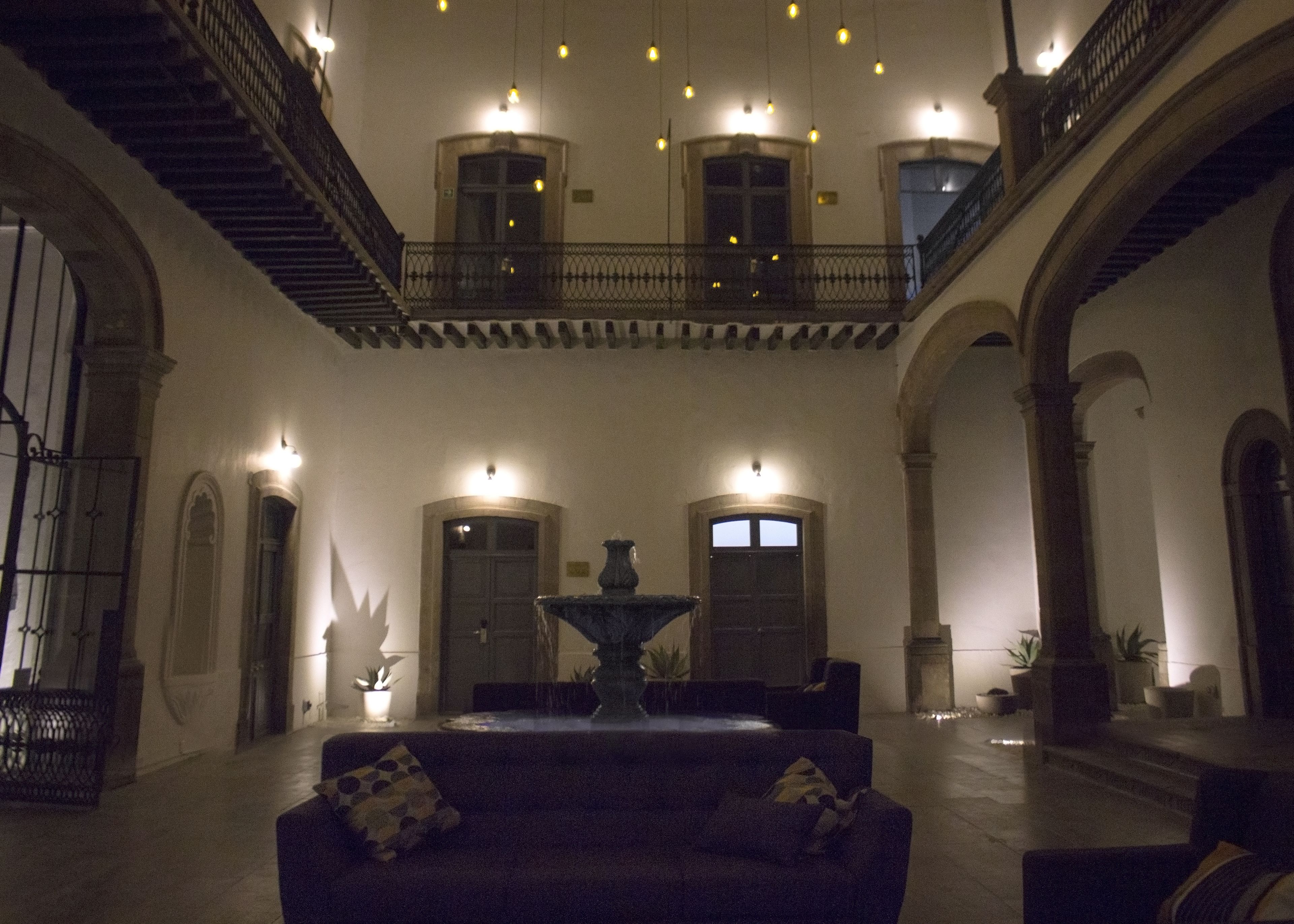 Een ruim interieur met een centrale fontein, een balkon en een trap.