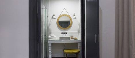 A modern bathroom with a round mirror, white sink, and a yellow stool.