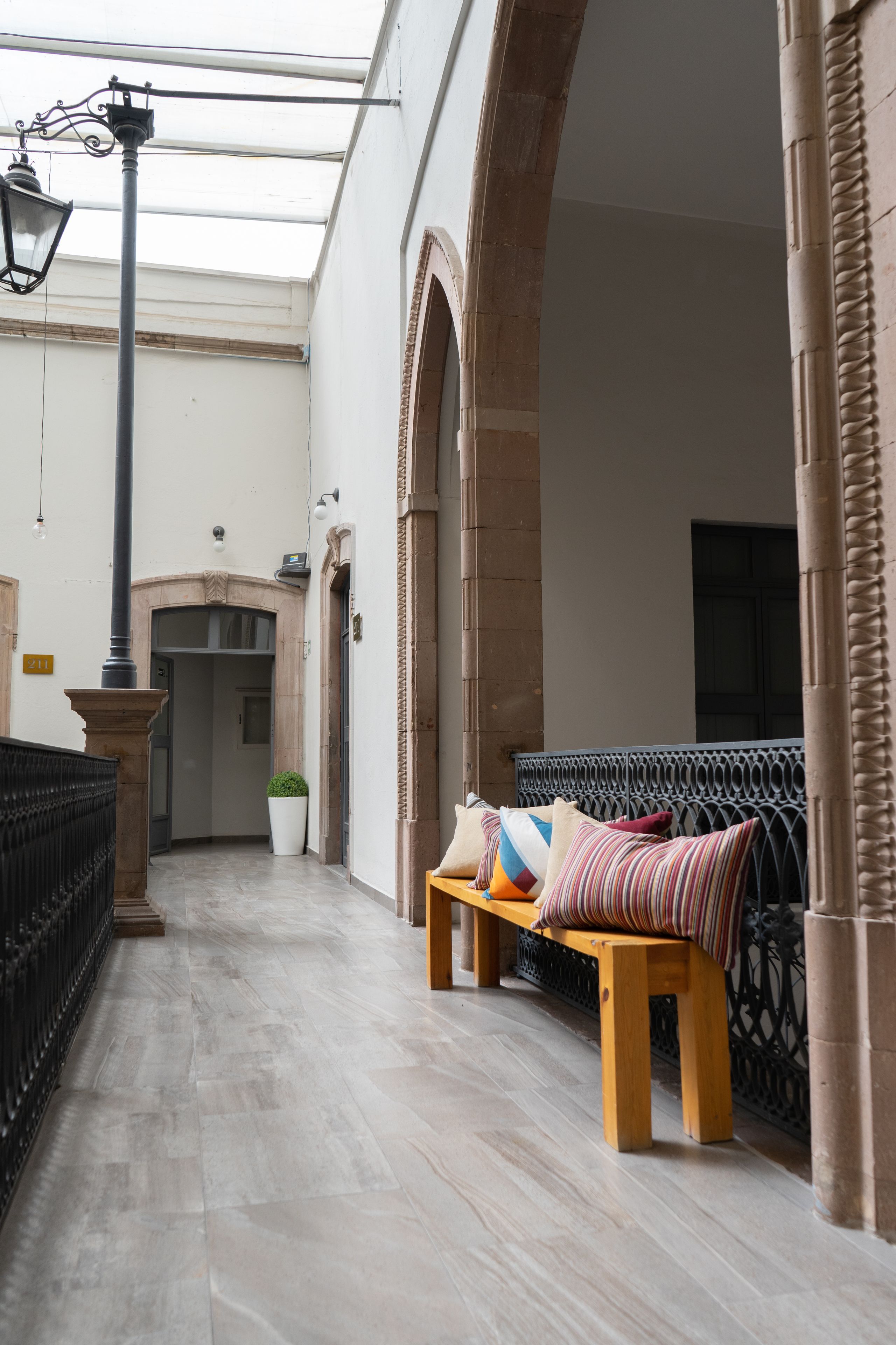 A corridor with a bench, a potted plant, and a street lamp.