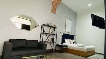 Una sala de estar moderna con un sofá, una mesa de centro, un televisor montado en la pared y una cama con cabecera.