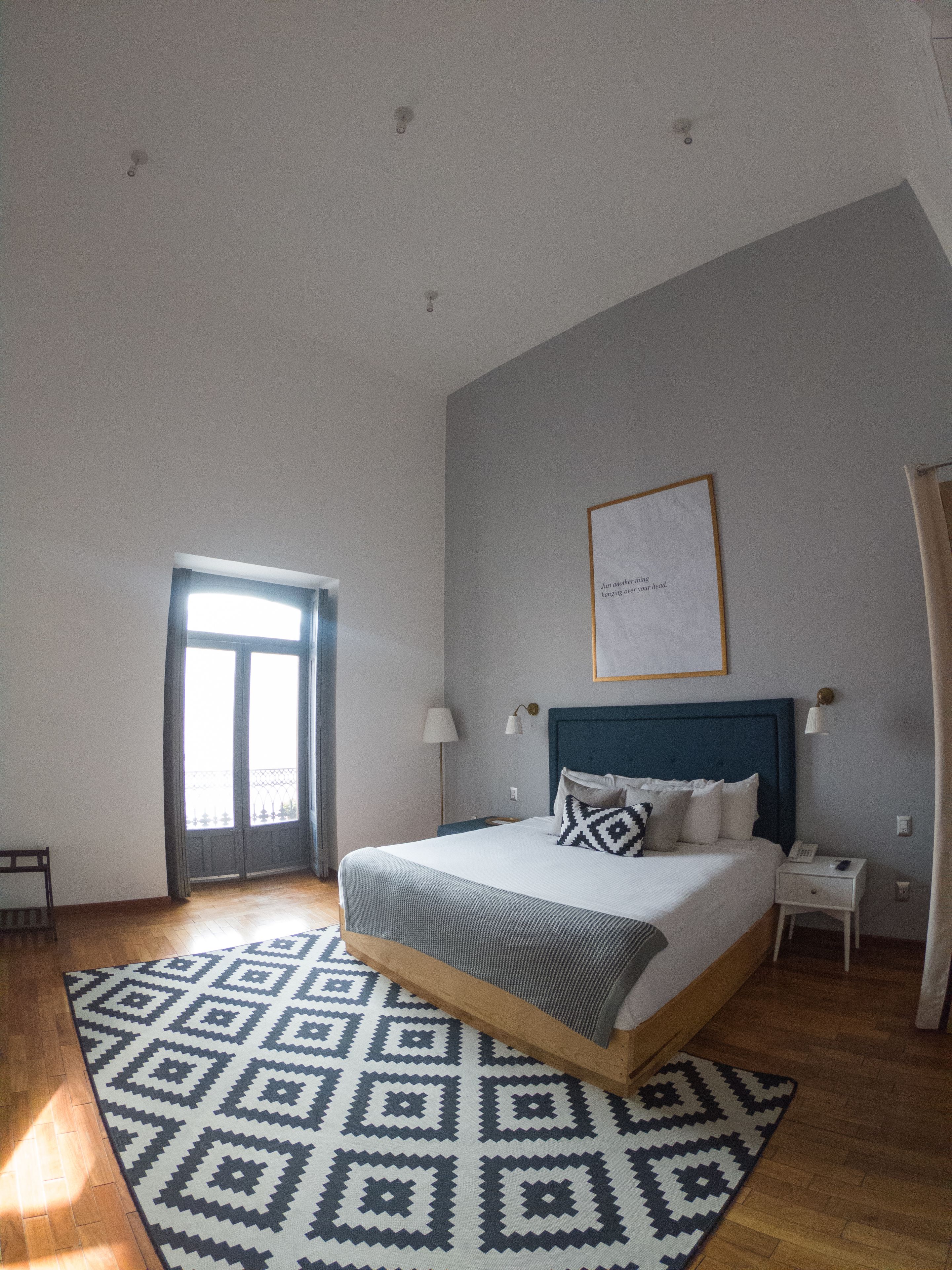 A spacious bedroom with a large bed, a bedside table, a nightstand, a framed picture on the wall, and a window with curtains.