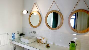 A bathroom with three wooden-framed mirrors, a glass sink, and a white tiled backsplash.