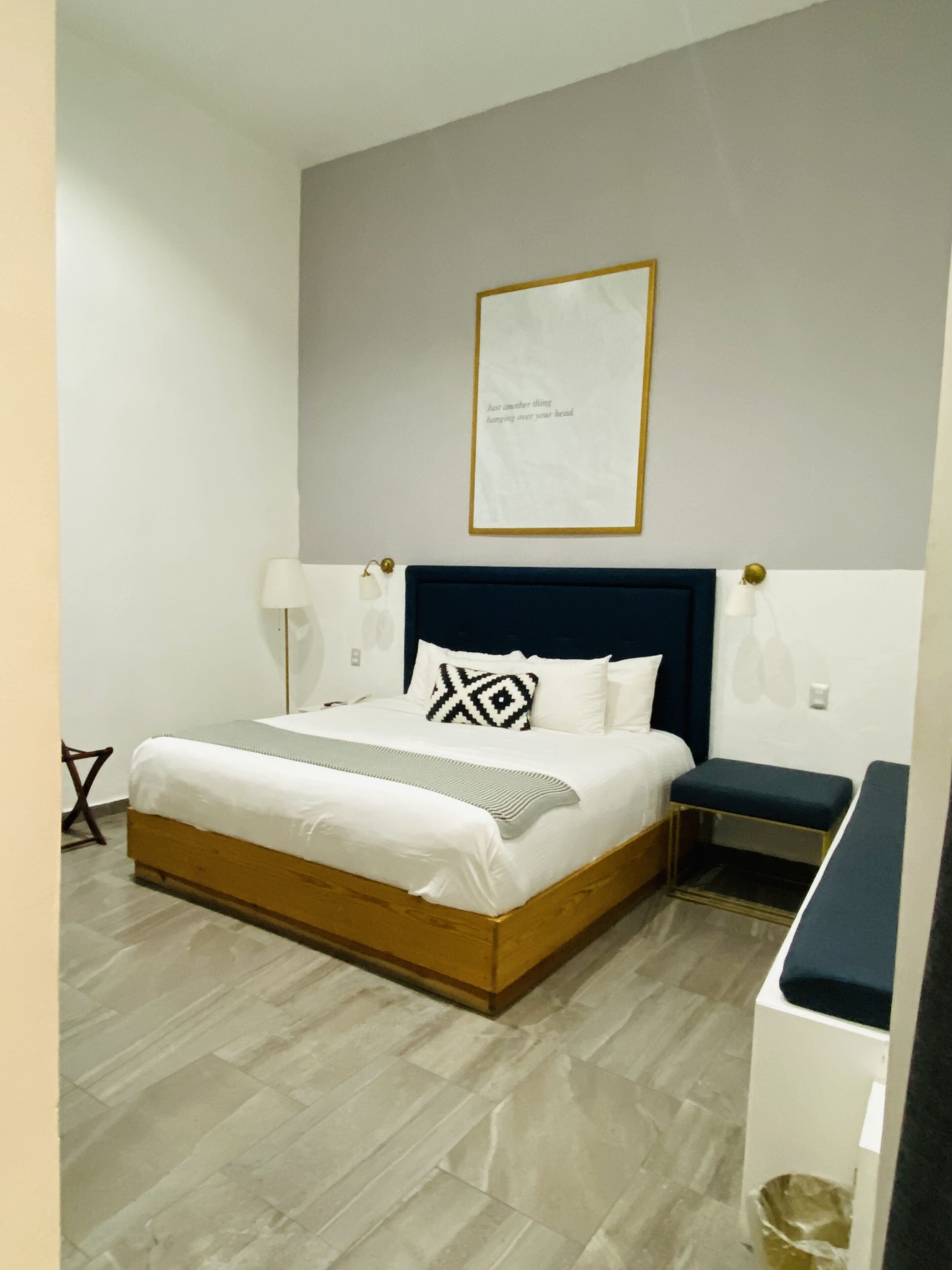 A neatly arranged bedroom with a bed, bedside tables, a wall-mounted picture, and a small stool.