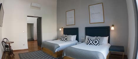 Habitación de hotel con dos camas, una mesita y una silla. Se observan cuadros en la pared y una lámpara en el techo.