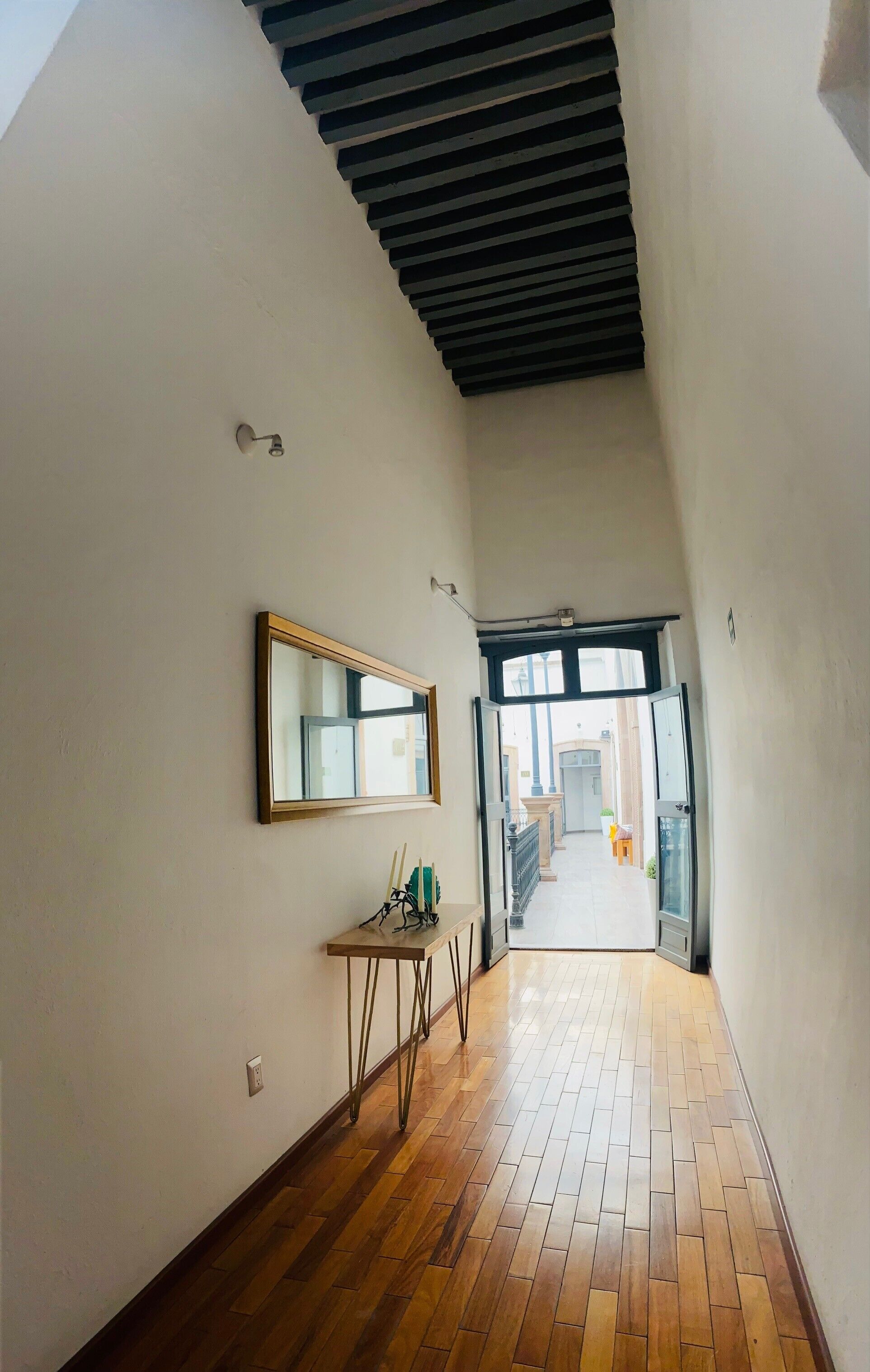 A narrow hallway with wooden flooring, a mirror on the wall, and a door leading to another room.