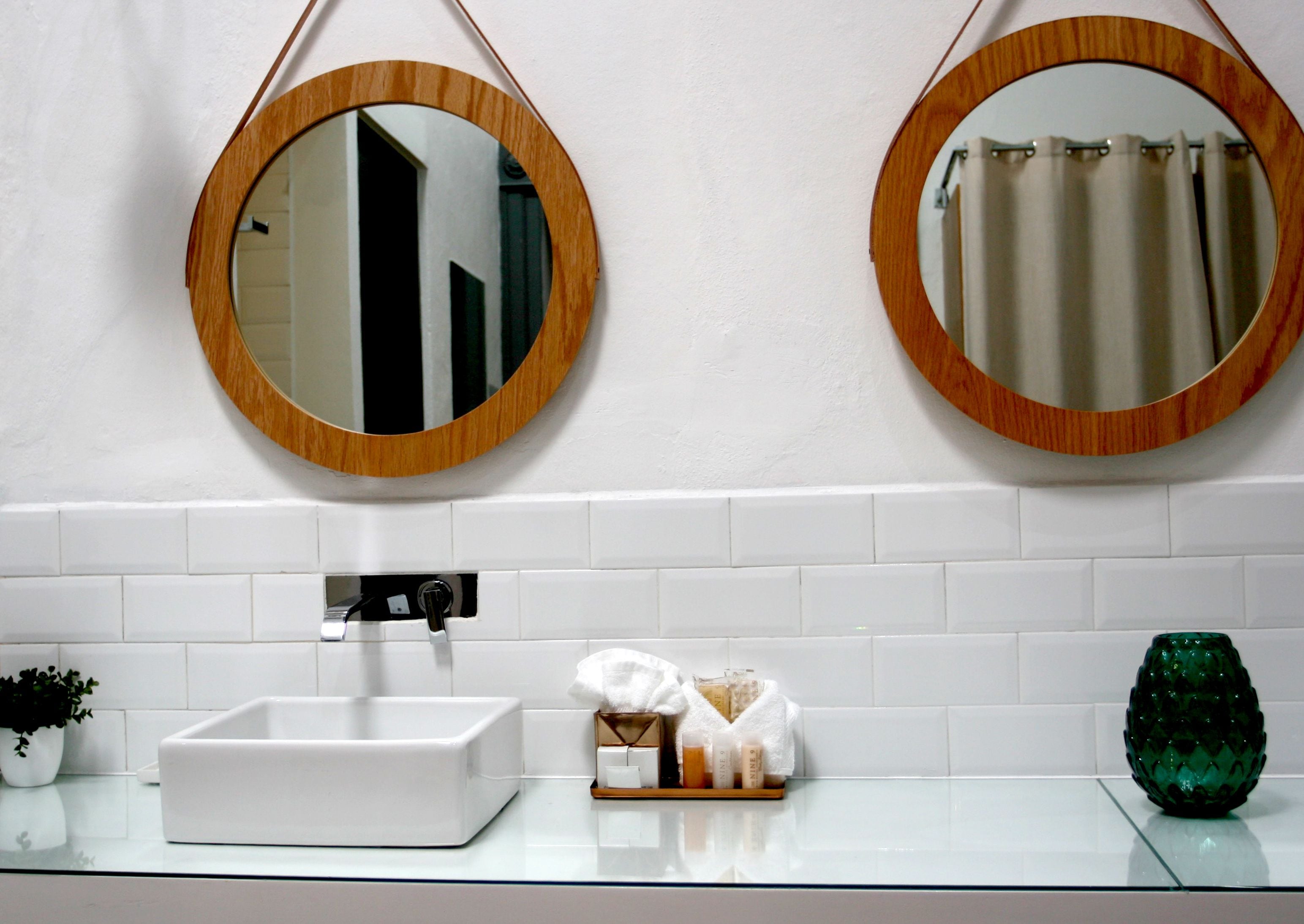 A bathroom with two wooden-framed mirrors, a white sink, and a glass countertop.
