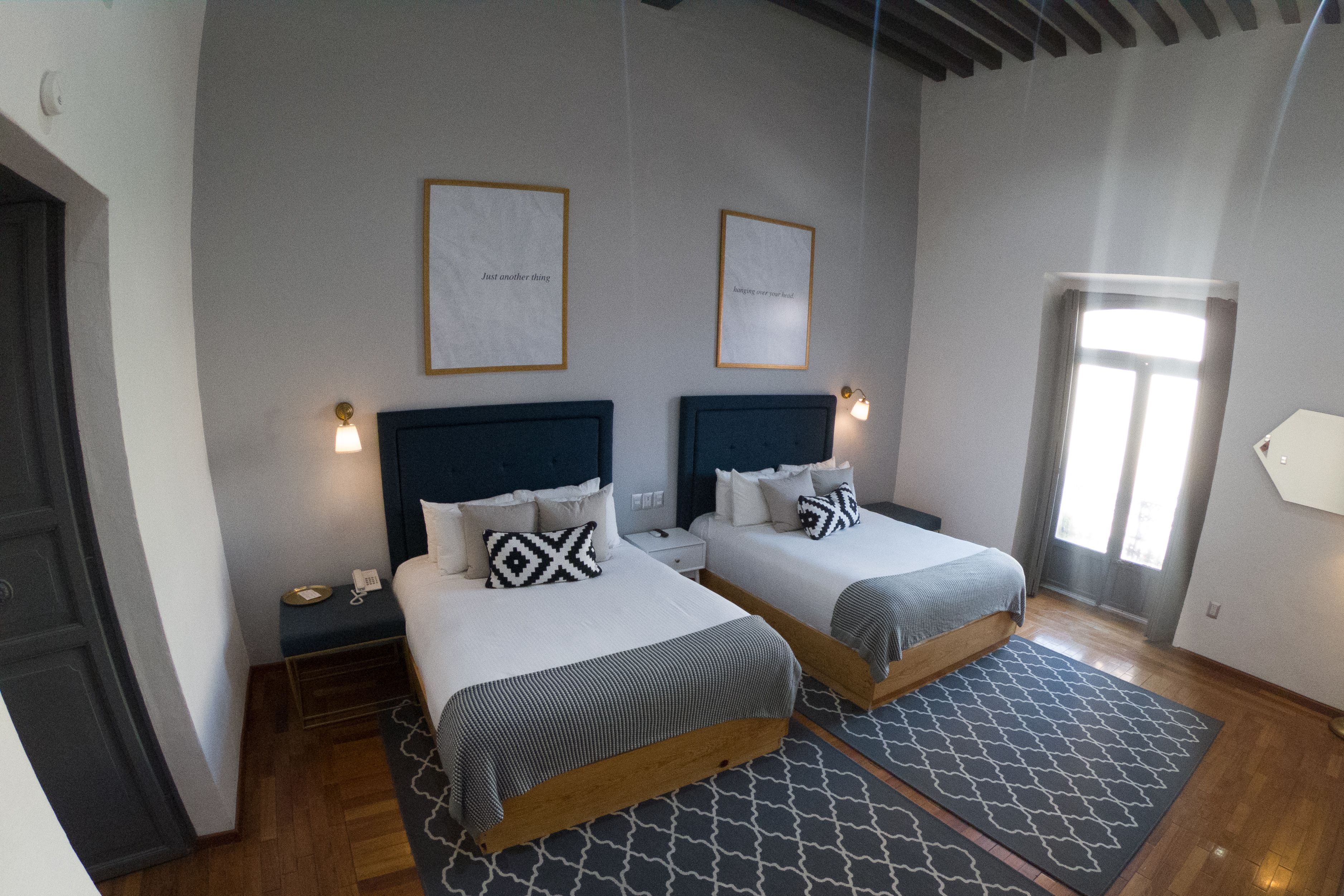 Una habitación de hotel con dos camas, una mesita de noche pequeña con una lámpara y una ventana con cortinas.
