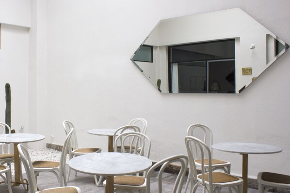 Une pièce aux murs blancs, avec plusieurs tables rondes et des chaises blanches.