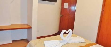 A hotel room with a bed, a wooden bench, a coat rack, and a door.