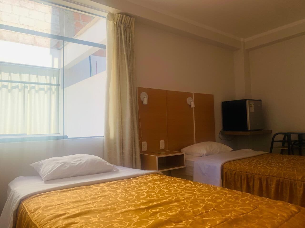 A hotel room with two beds, a TV, a desk, and a window with curtains.