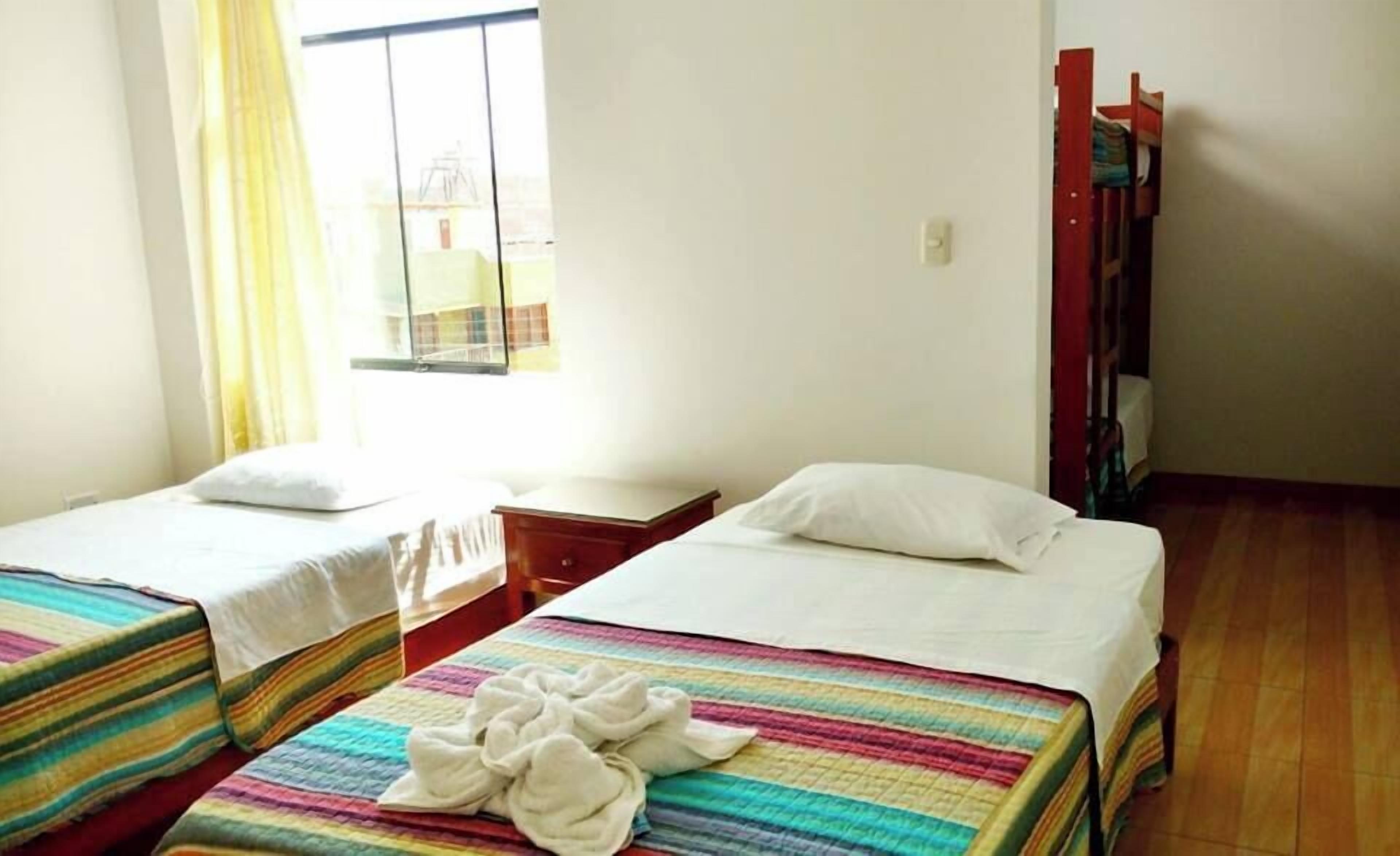 A hotel room with two single beds, a wooden nightstand, a window with curtains, and a wooden chair.