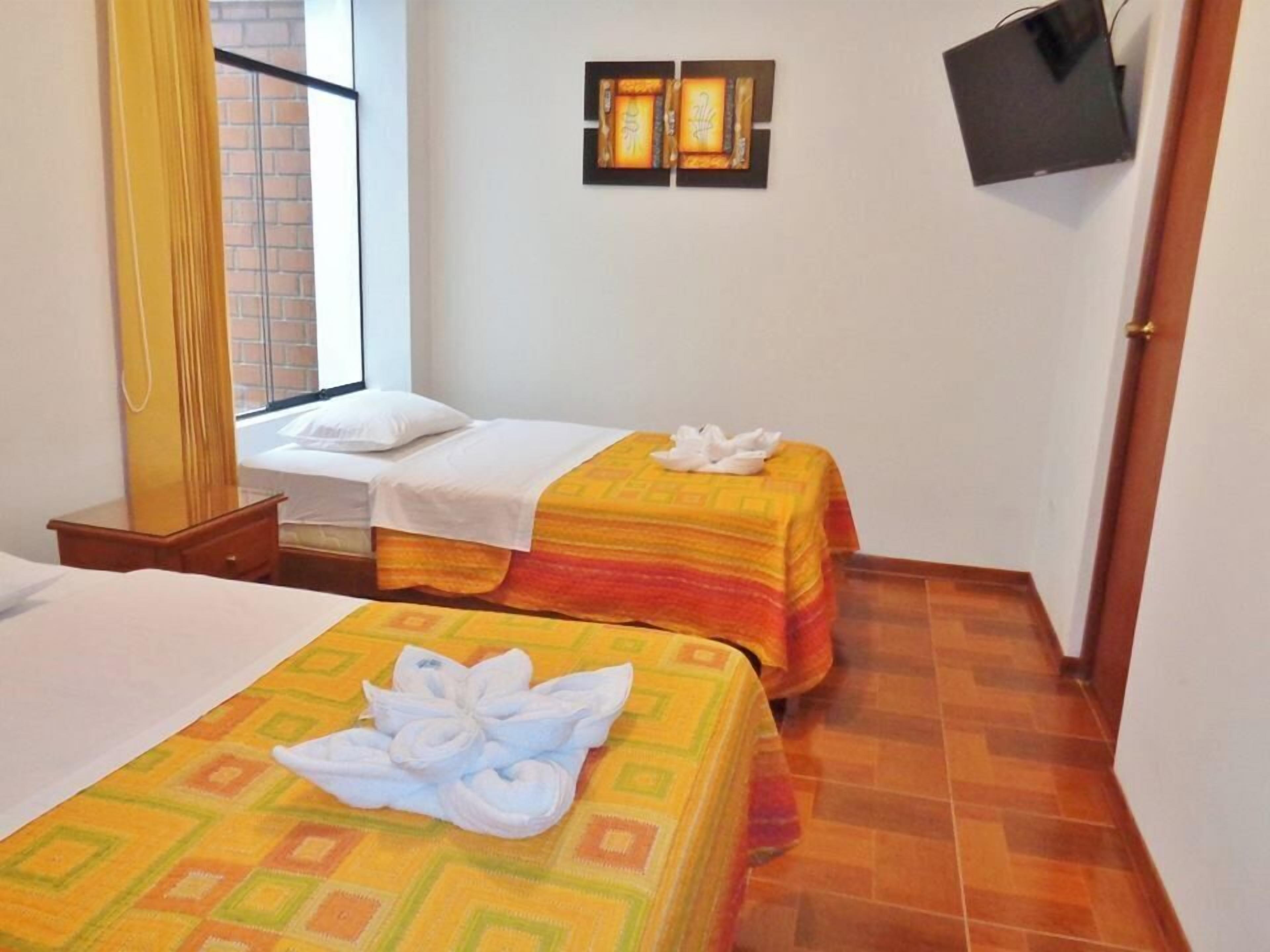 A hotel room with two beds, a TV mounted on the wall, and a window with a view of a brick wall.