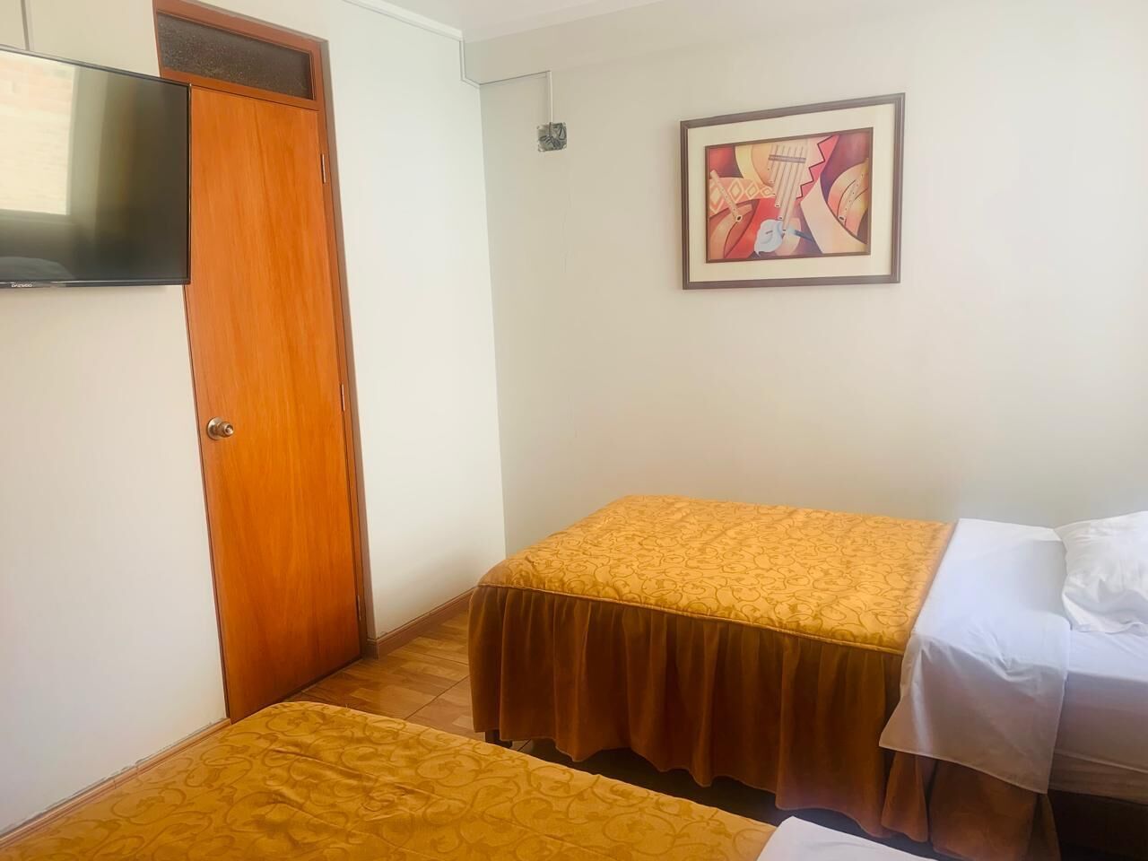 A room with a bed, a wardrobe, a television, and a framed artwork on the wall.