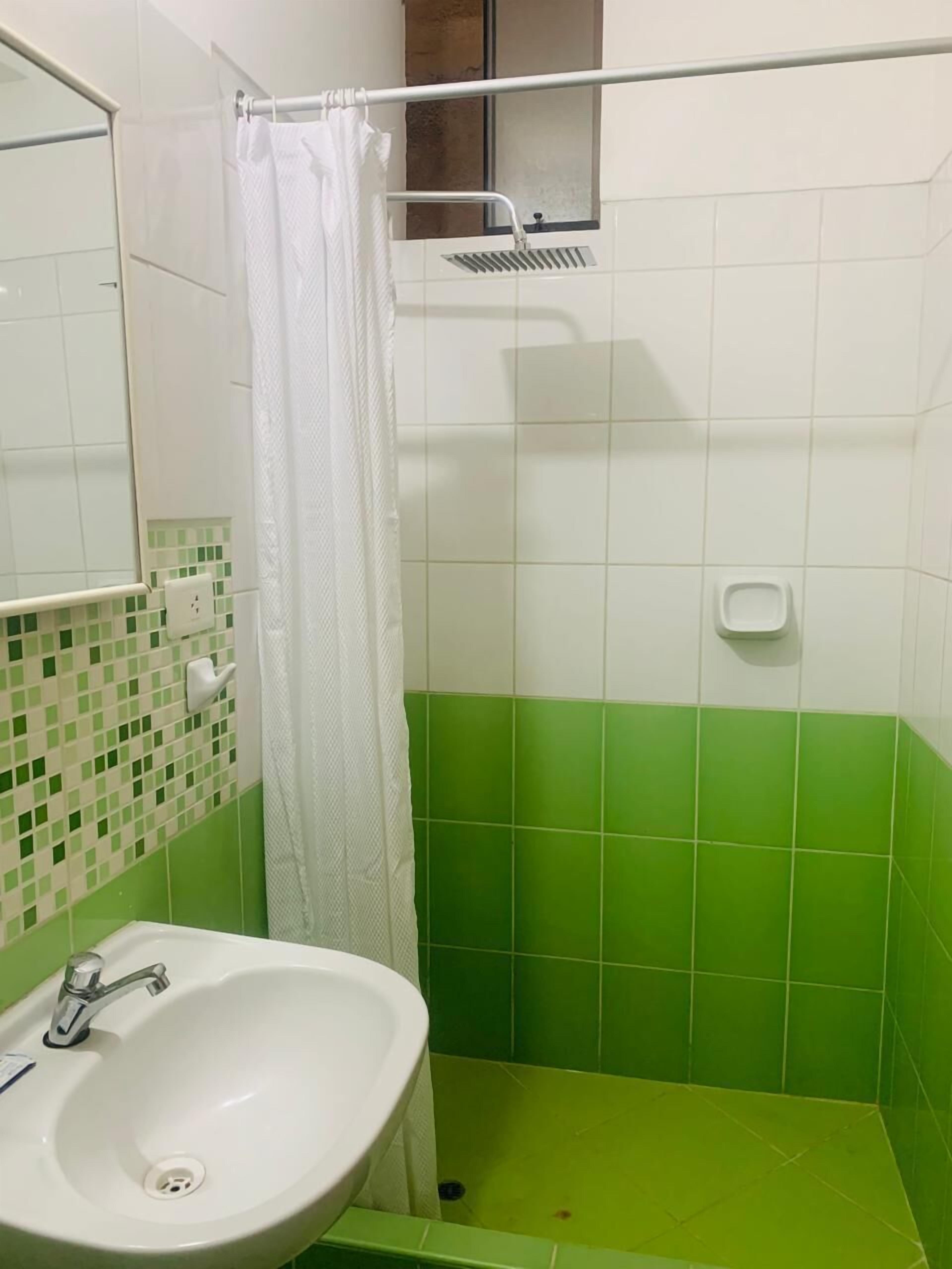 Um banheiro com pia branca, paredes azulejadas em verde e branco, cortina de chuveiro e uma pequena janela.