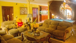 Een woonkamer met een pooltafel, een plafondventilator en een teddybeer.