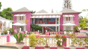 A pink and white two-story house with a balcony, potted plants, and outdoor furniture. - PinkHibiscus Guest House (Montego Bay)
