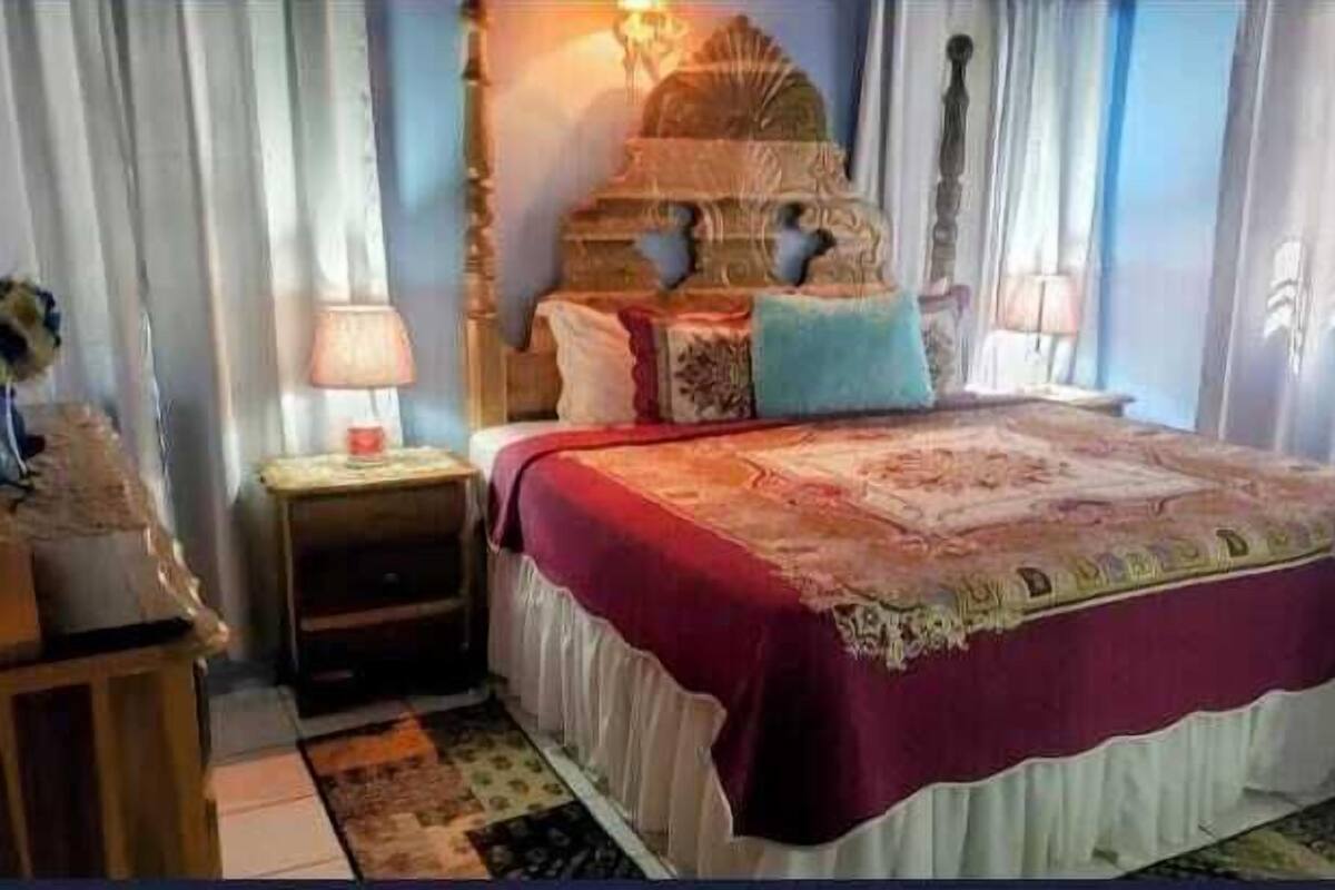 A bedroom with a bed, a nightstand, a lamp, and a decorative headboard.