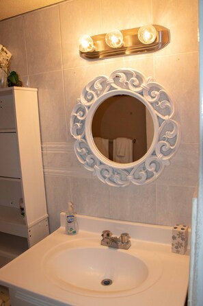 A bathroom with a white sink, a decorative mirror with an ornate frame, and a light fixture above the mirror.
