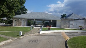 A modern building with a stone facade, a covered entrance, and a paved driveway leading to a gated entrance.