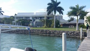 A marina with boats docked, a stone wall, and a building with a flat roof in the background. - Seawind On the Bay - Apartments (Montego Bay)