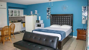 A bedroom with a bed, a chair, a desk, and a kitchenette. - Seawind On the Bay - Apartments (Montego Bay)