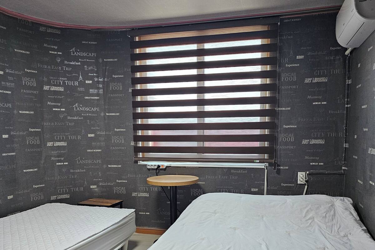 Ein Zimmer mit zwei Einzelbetten, einem kleinen runden Tisch und einem Fenster mit Jalousien.