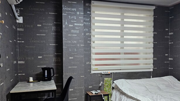 A bedroom with a bed, a desk with a chair, a window with blinds, and a wall with printed text. - Mirim Motel (Gyeongju)