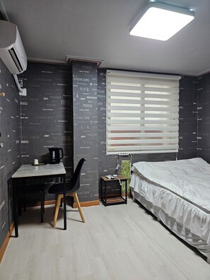 A bedroom with a bed, a desk with a chair, a window with blinds, and a wall with printed text. - Mirim Motel (Gyeongju)