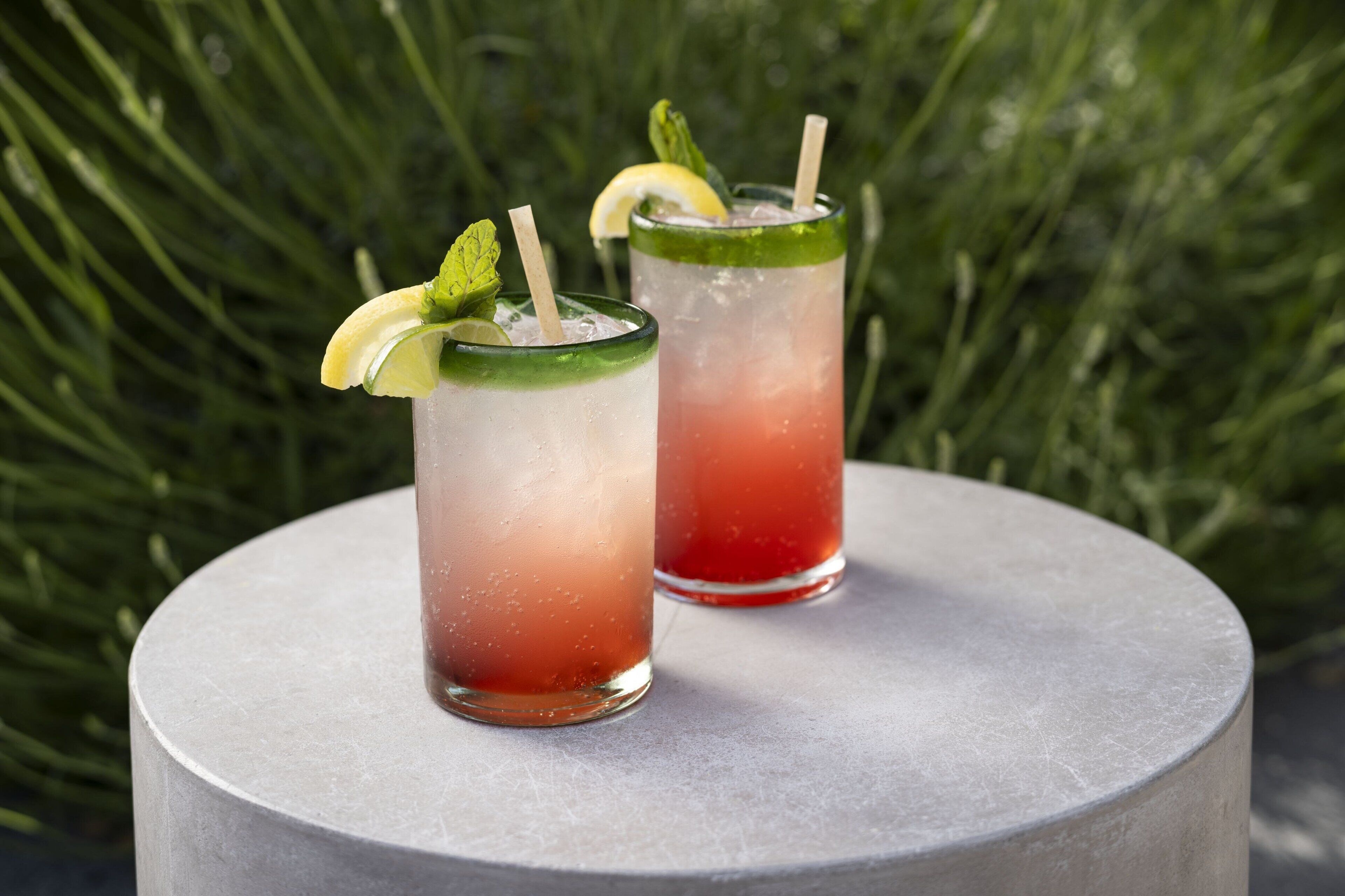 Two glasses of iced drinks with lime and mint garnish on a round table.